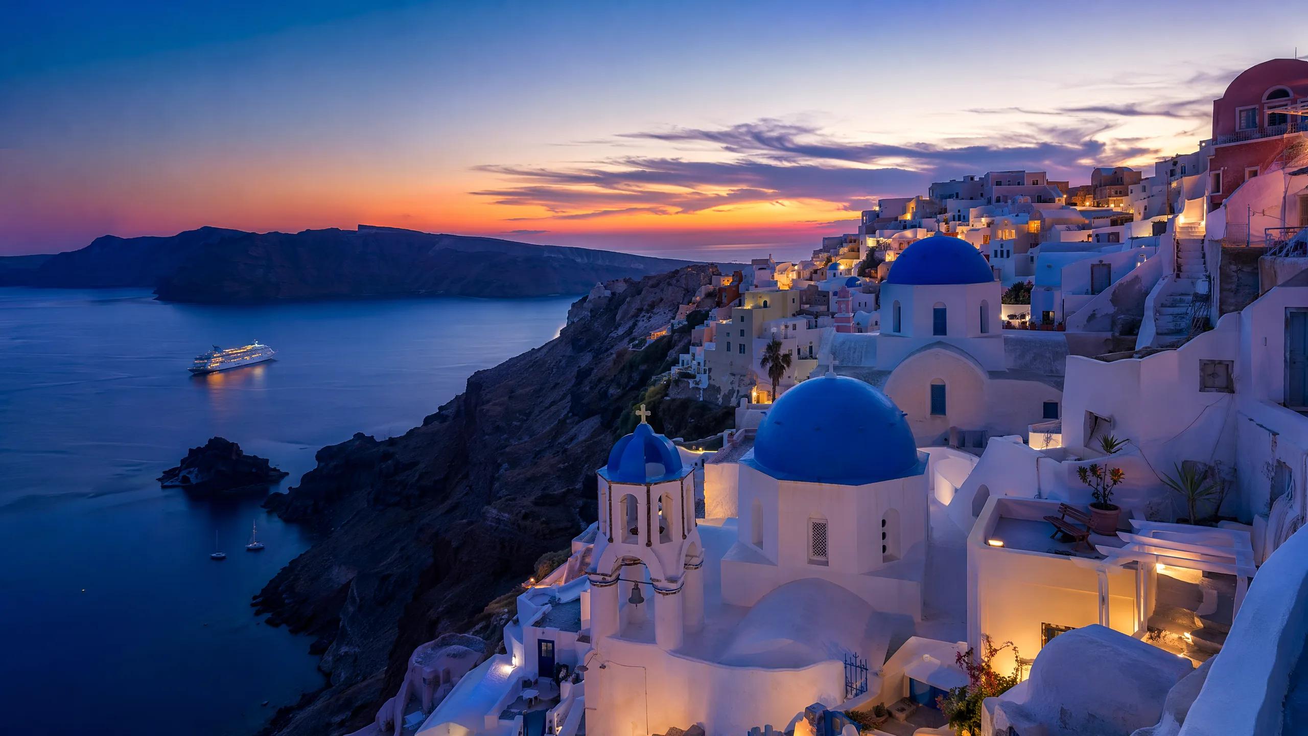 Santorini Greece at sunset with white-washed buildings and blue-domed churches c