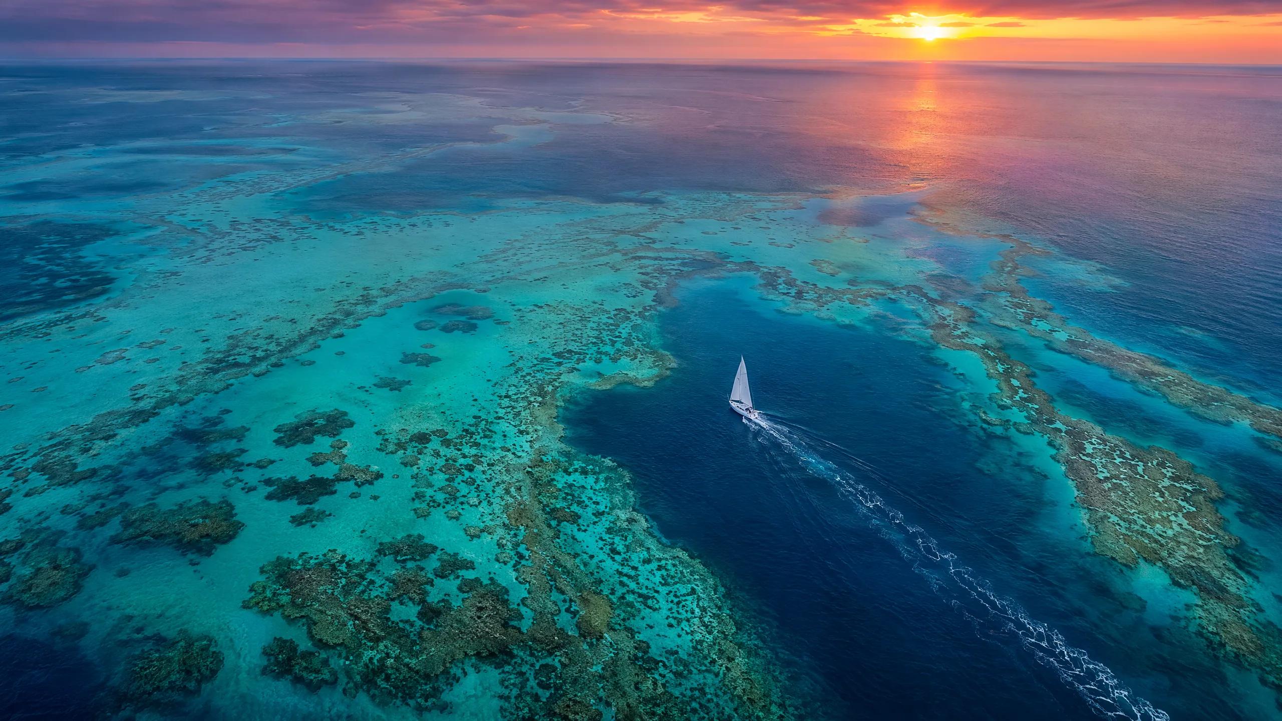 Aerial drone photograph of a lone white sailboat sailing over turquoise coral re
